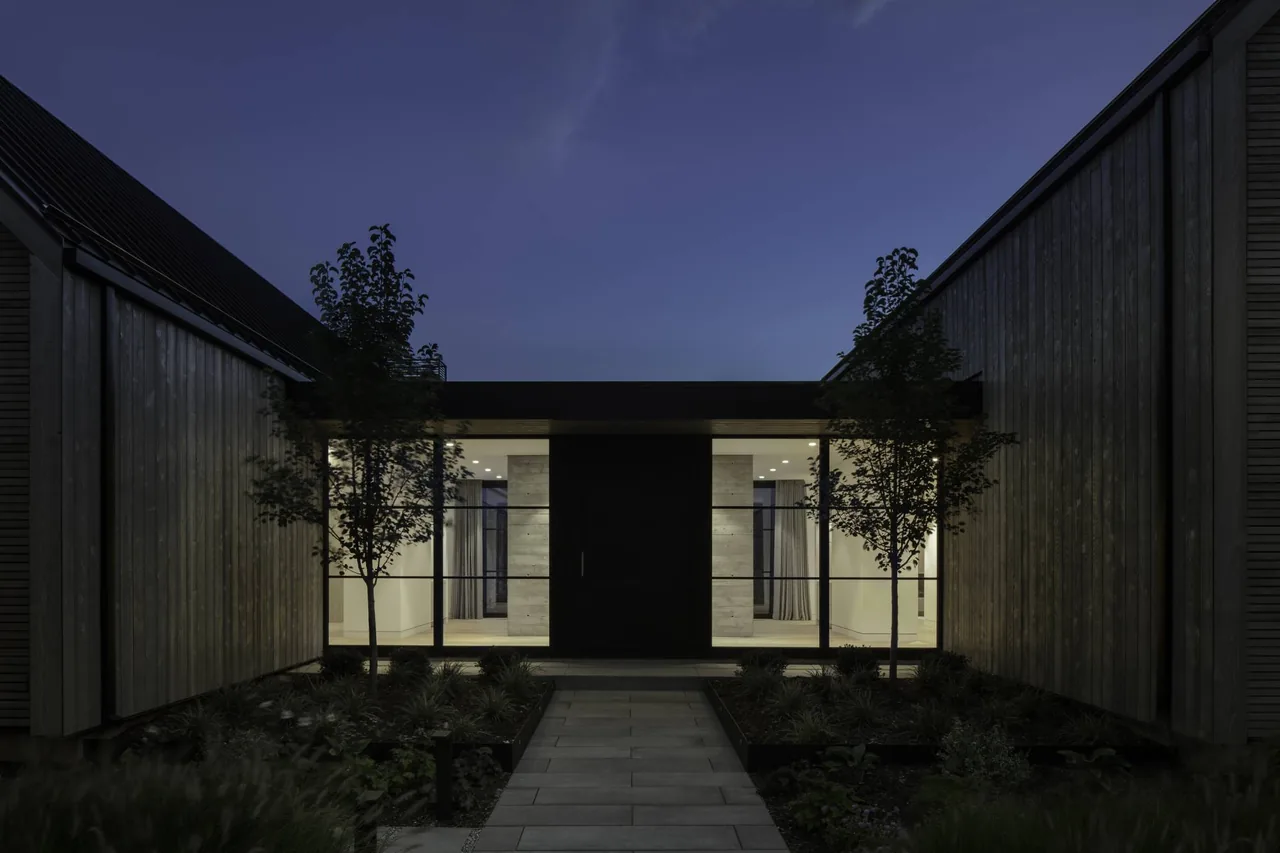 Entrance of Linden Grove by Studio B Architects featuring vertical wooden siding and large black-framed windows at night.