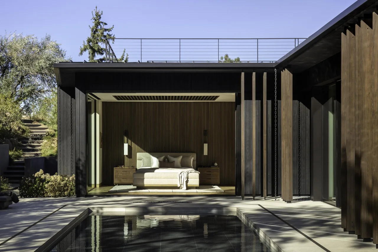 A modern bedroom opens completely to an outdoor pool area with vertical wooden slats as a back wall feature.