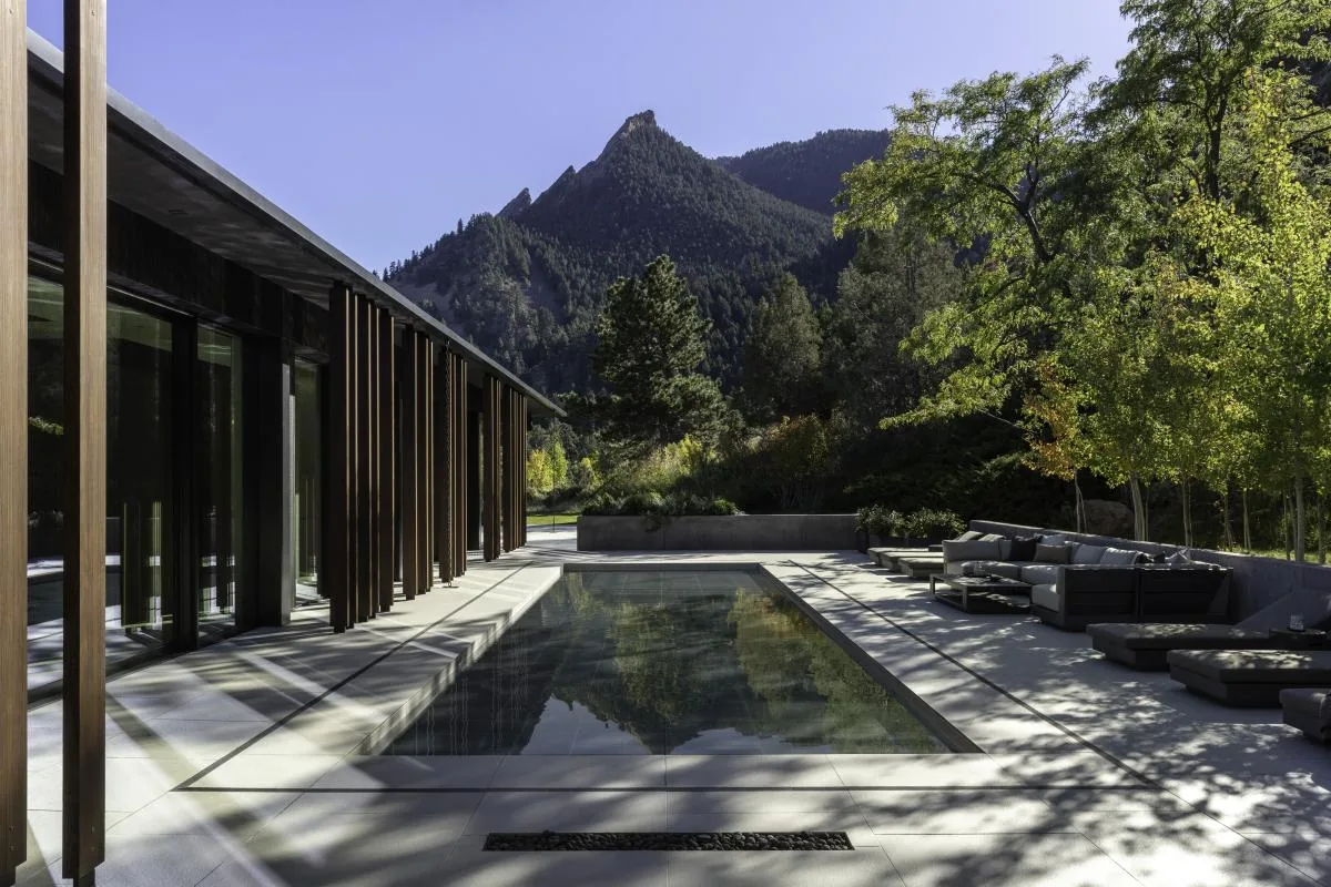 Modern rectangular outdoor pool with adjacent patio seating and vertical wooden slats on the building exterior.