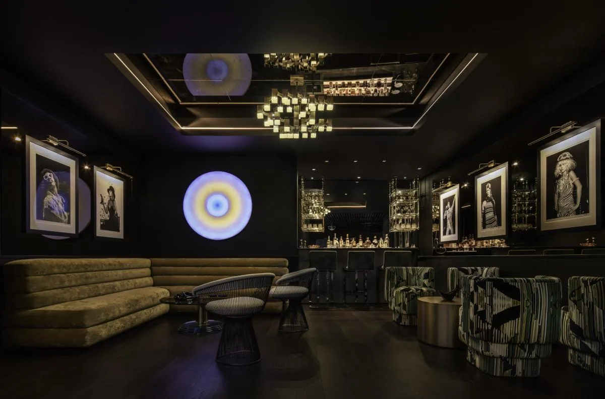 Interior of a dark lounge featuring modern seating, artwork, and a bar area with metallic finishes.