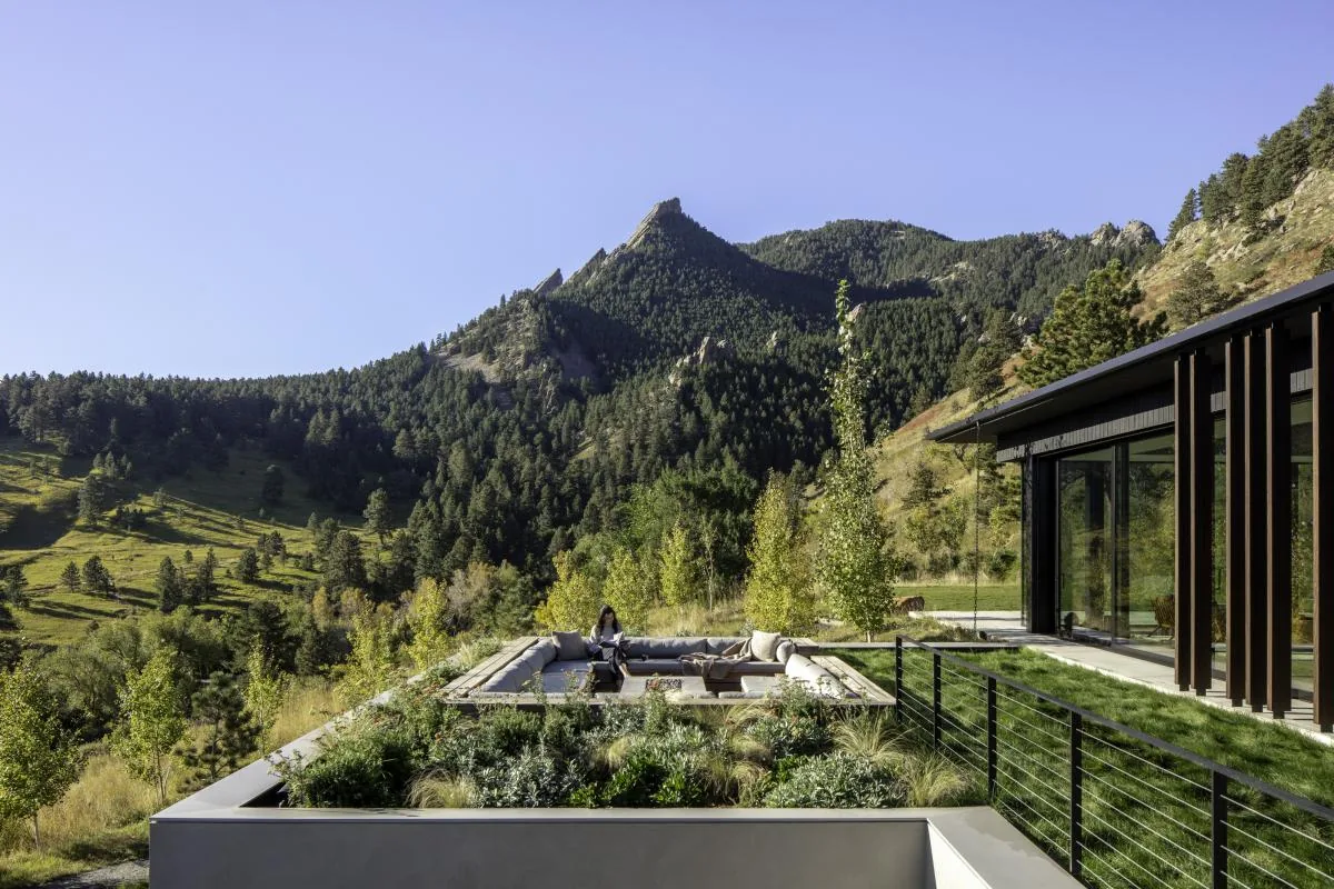 Sunken outdoor seating area with landscaping next to a modern house with tall vertical window mullions.