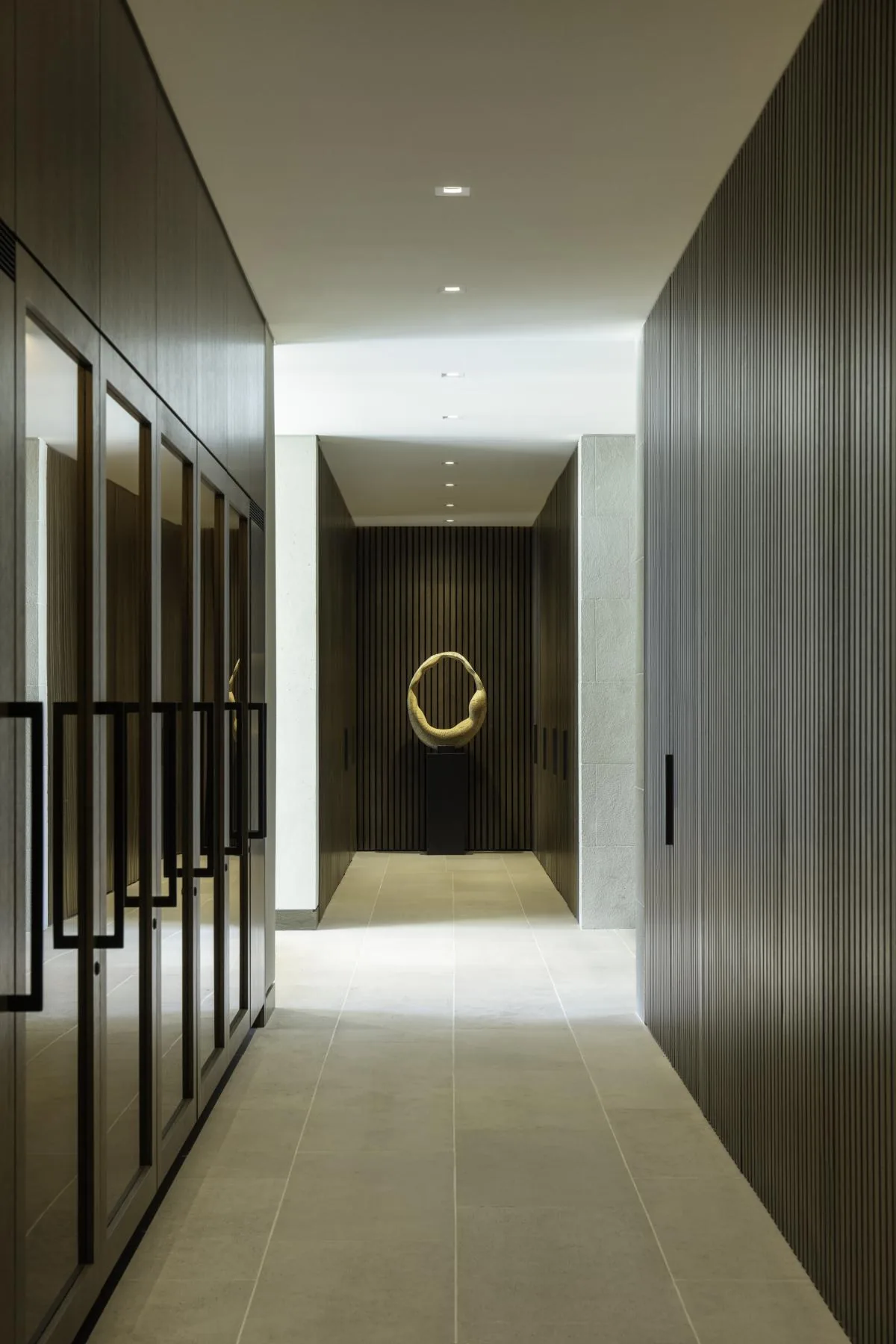 Hallway with dark vertical wood paneling and light tiled floor leading to a sculpture on a pedestal.