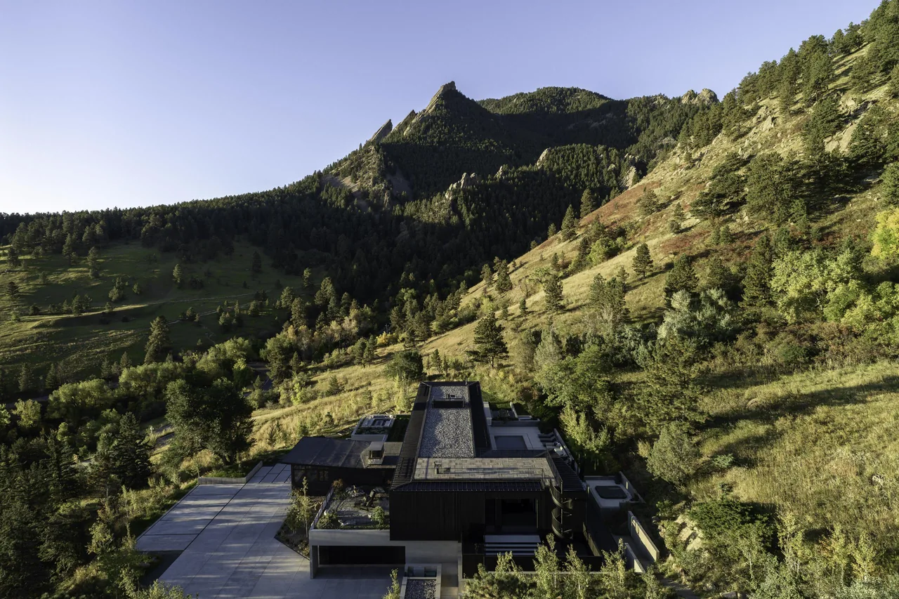 Modern house located on a sloped hillside with extensive natural landscape and mountains behind.
