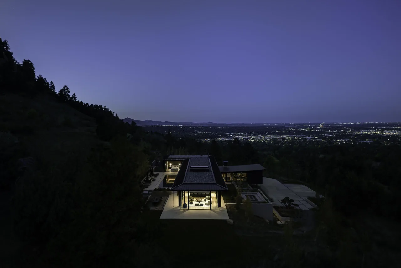A nighttime aerial photo captures the Panorama House with illuminated interior spaces on a hillside.