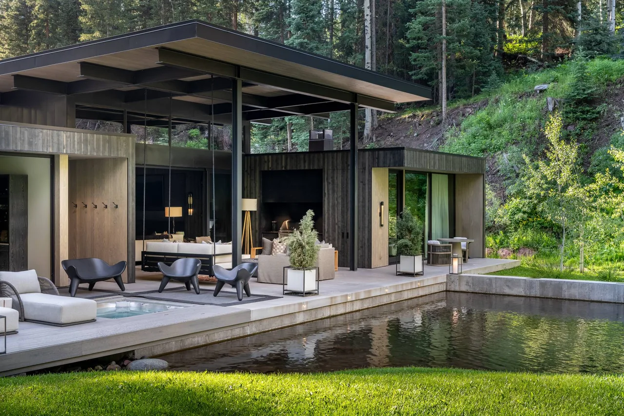 Conundrum Creek house features flat roof and floor-to-ceiling glazing overlooking a reflecting pond and outdoor seating area.