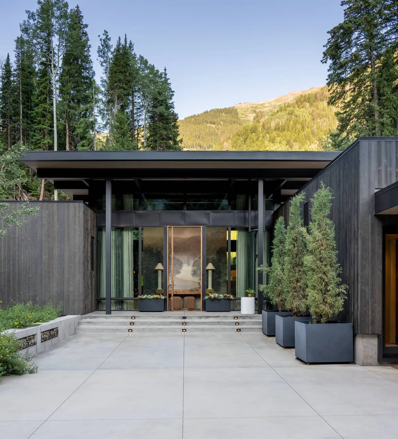 Entrance of a modern house featuring floor-to-ceiling glazing and a flat roof with mountain views.