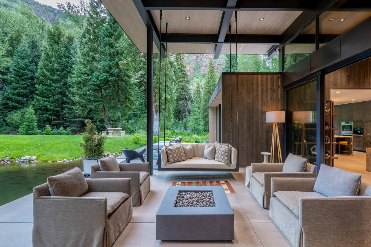 Outdoor patio seating space with hanging sofa and firepit table by a reflective creek, designed by Studio B Architects for Conundrum Creek.