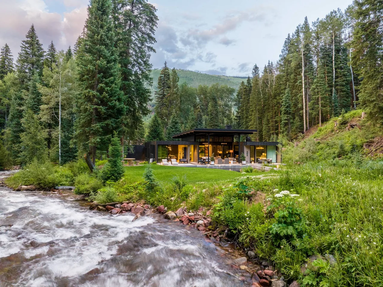 Conundrum Creek features a modern flat-roof house with expansive glazing situated by a creek and forest landscape.