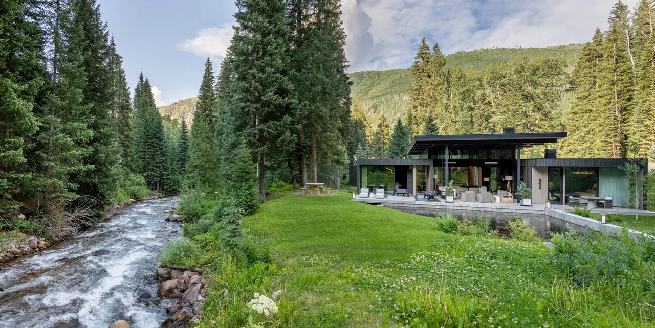 Conundrum Creek residence features floor-to-ceiling glazing with a flat roof overlooking a creek and surrounding trees.