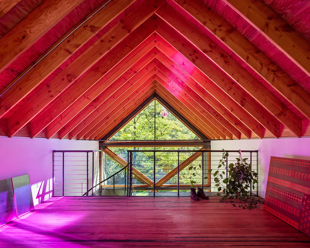 Loft area with exposed beams and a shed roof featuring a triangular picture window and wood flooring.