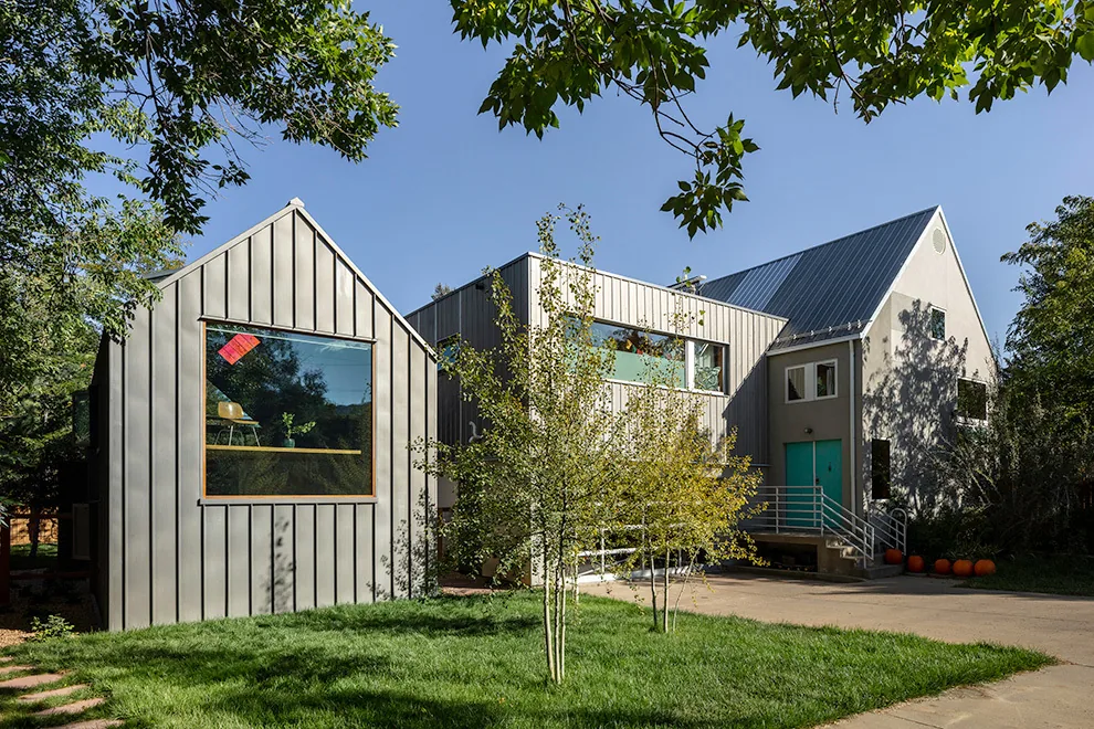 Exterior view of a residential building featuring vertical metal siding and gable roofs with large windows.