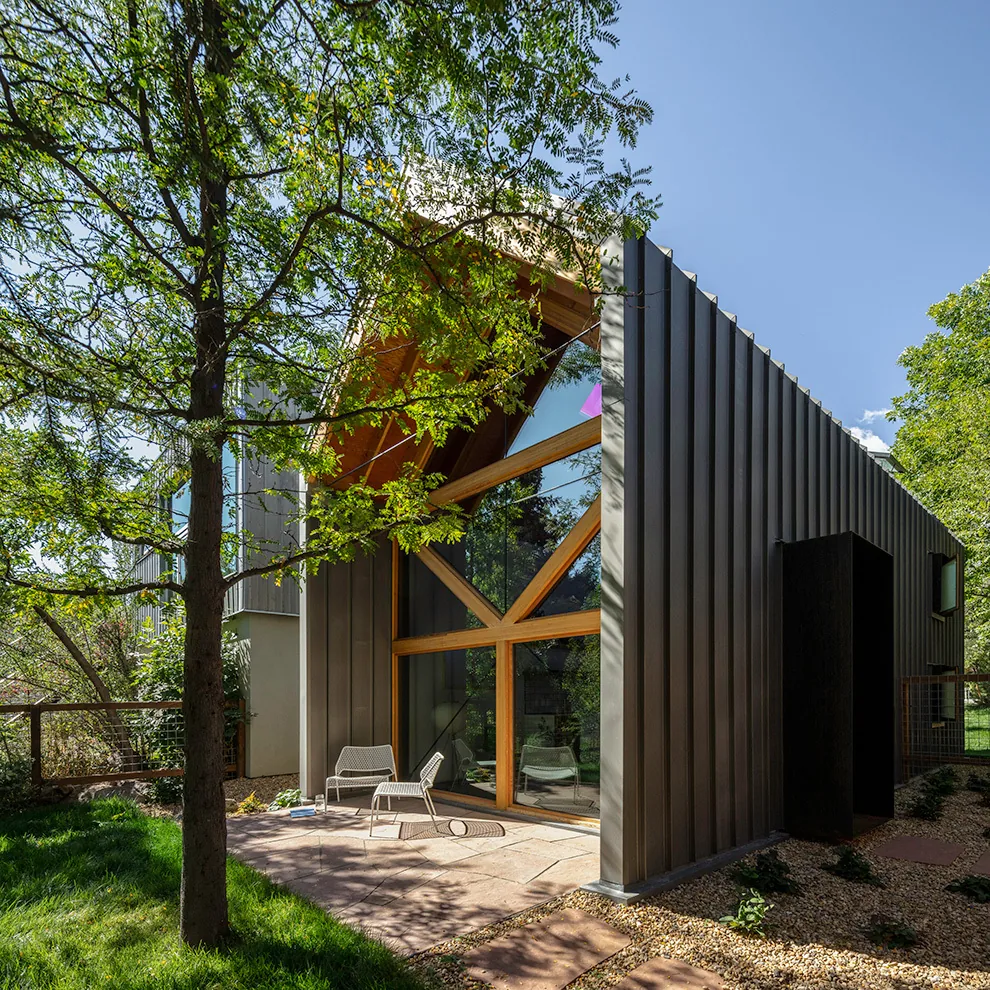 Modern ADU with shed roof and large triangular window framed in wood, featuring vertical metal siding and an outdoor patio area.