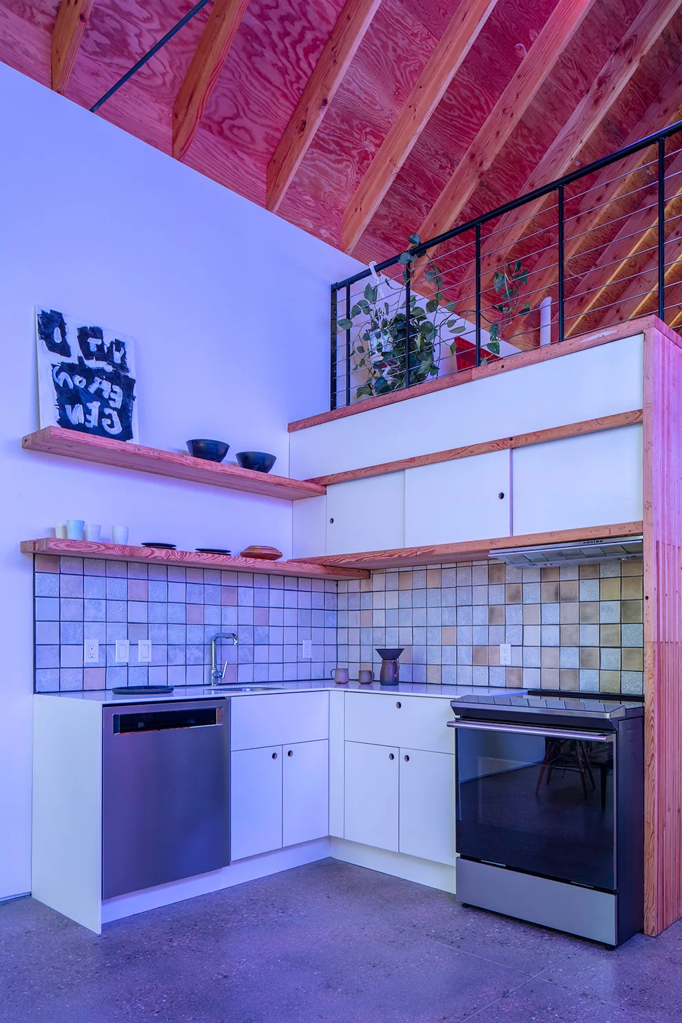 Kitchen with tiled backsplash, floating wood shelves, and stainless steel appliances below an open wood-beamed ceiling.