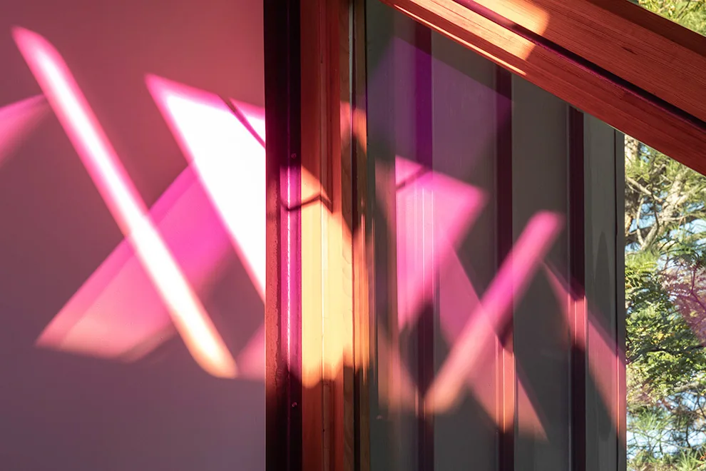 Colorful sunlight reflections from a triangular window cast on an interior wall and door frame.
