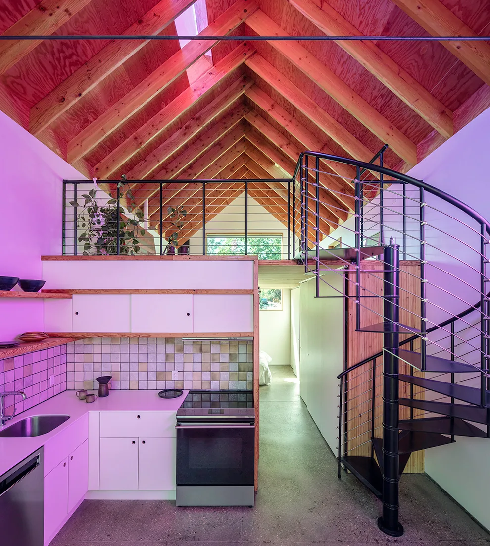 Loft kitchen with natural wood vaulted ceiling and black spiral staircase under triangular windows.