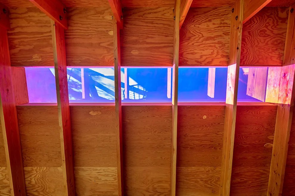 Exposed wood ceiling beams highlight a horizontal skylight with colorful light reflections in this A.D.U. project.