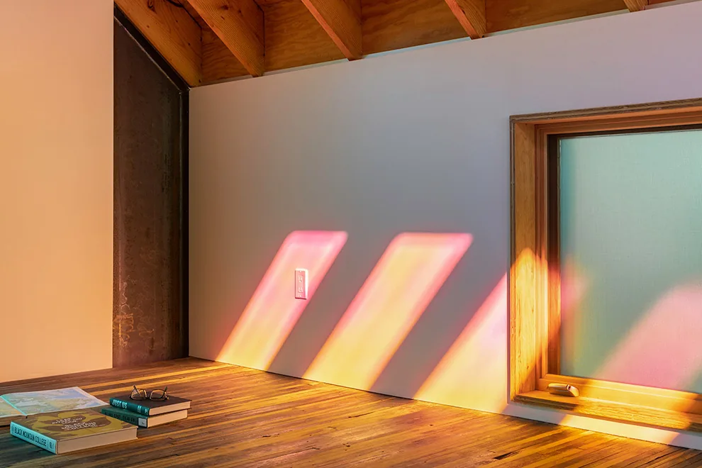 Sunlight creates colorful patterns on floor and wall beneath exposed wood beam ceiling in ADU project.