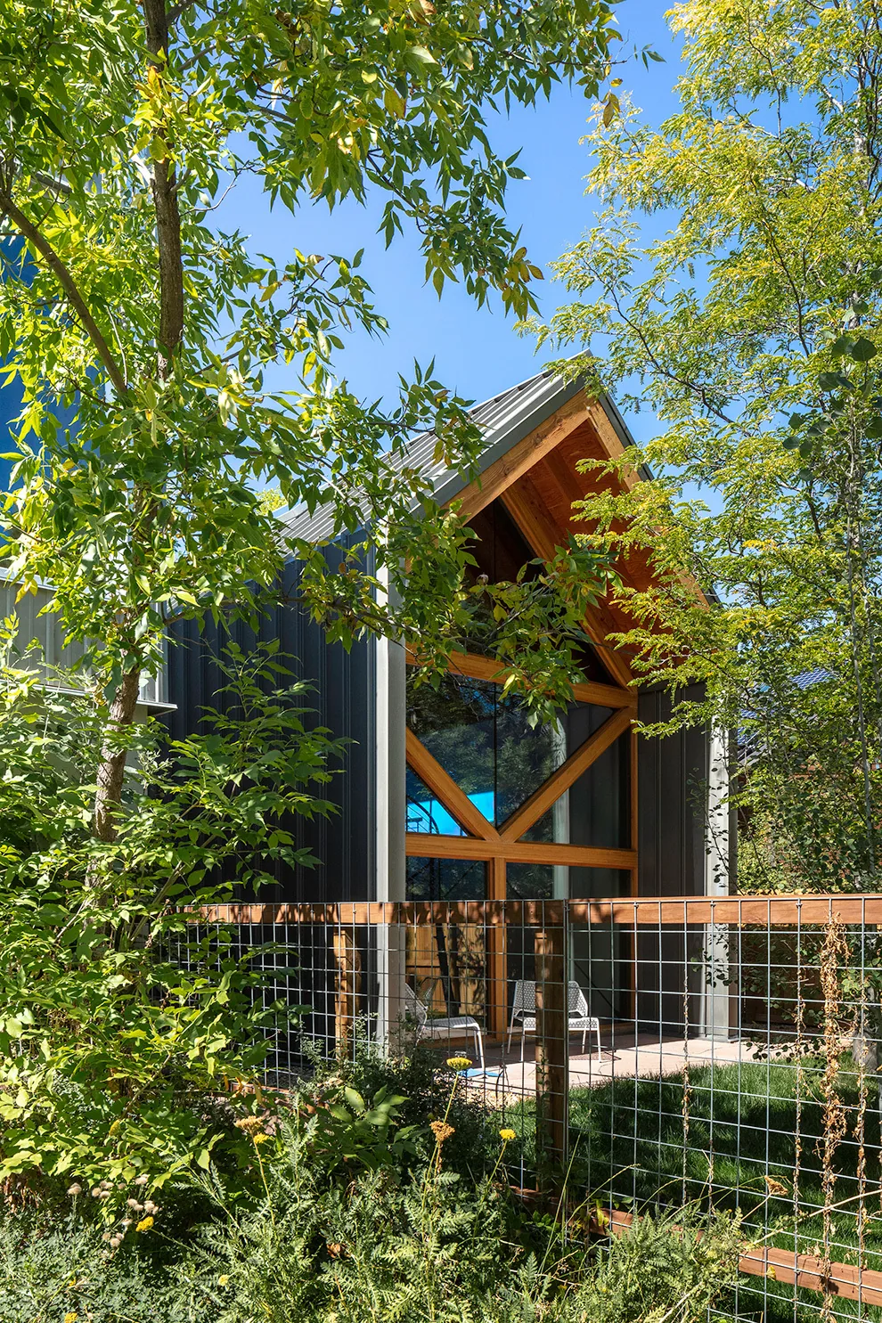 The A.D.U. features vertical metal siding, a gable roof, and large triangular wood-framed windows opening to a small patio.