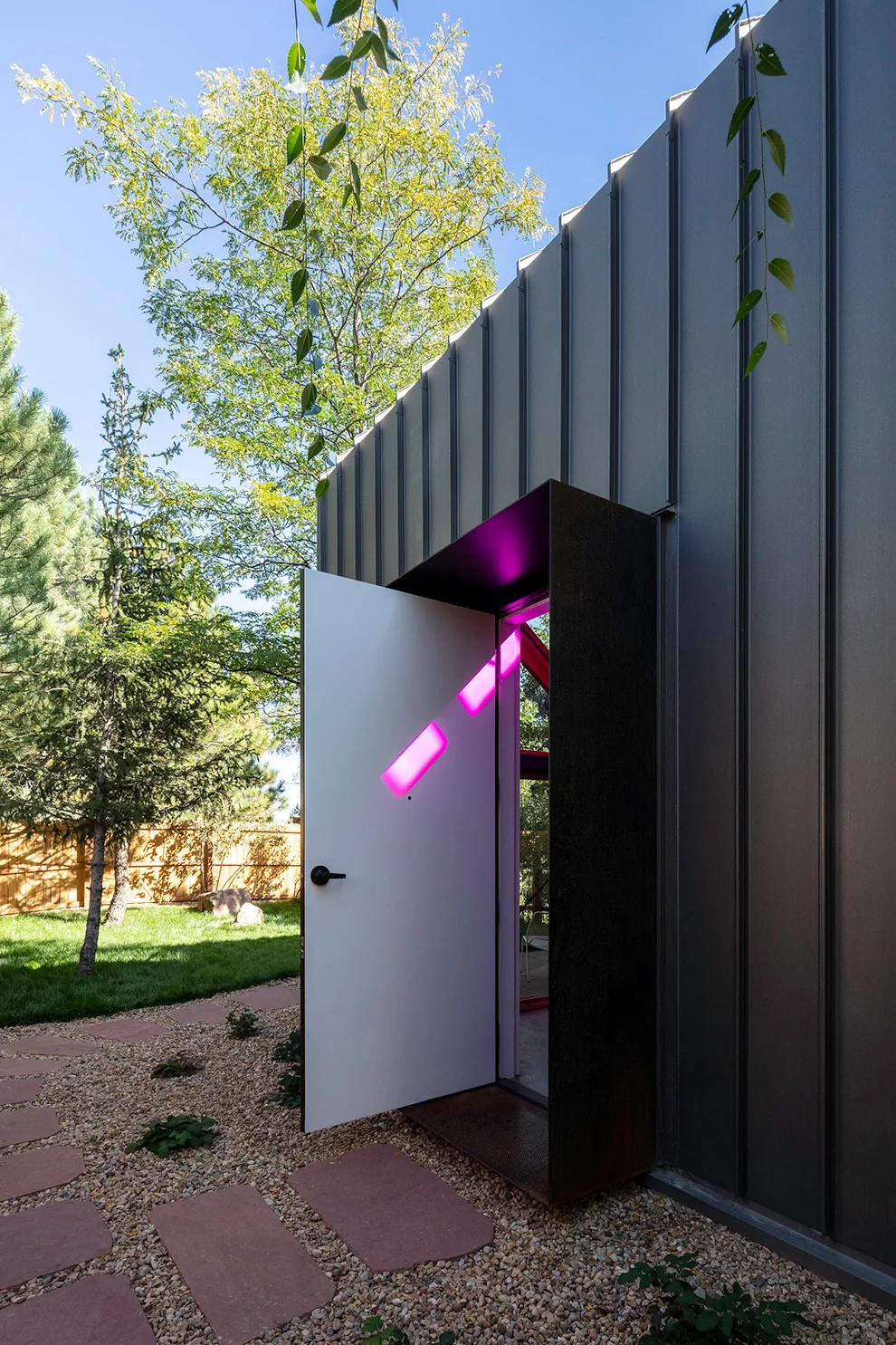 Open white door in a modern metal-sided exterior shows bright pink sunlight on the interior wall.