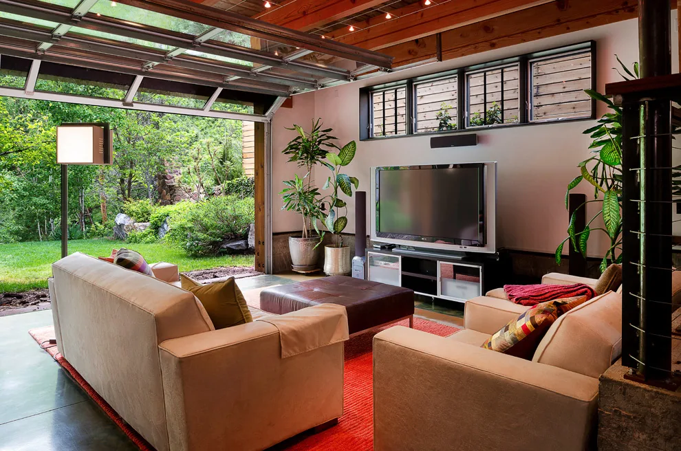 Living room with large glass spring-open garage door that opens to a garden.