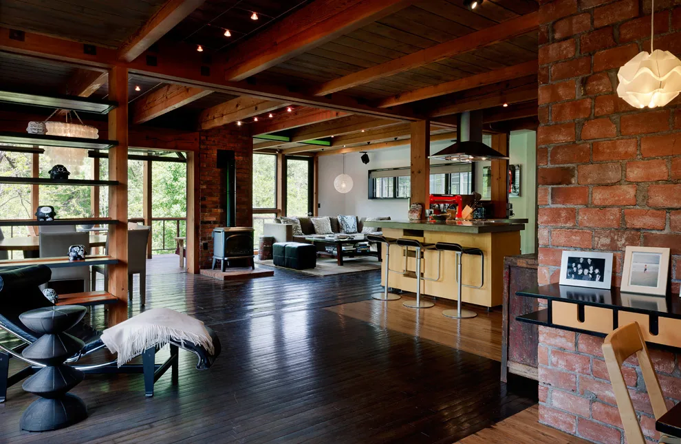 Open plan living space featuring exposed wood beams, brick accent wall, and large windows.