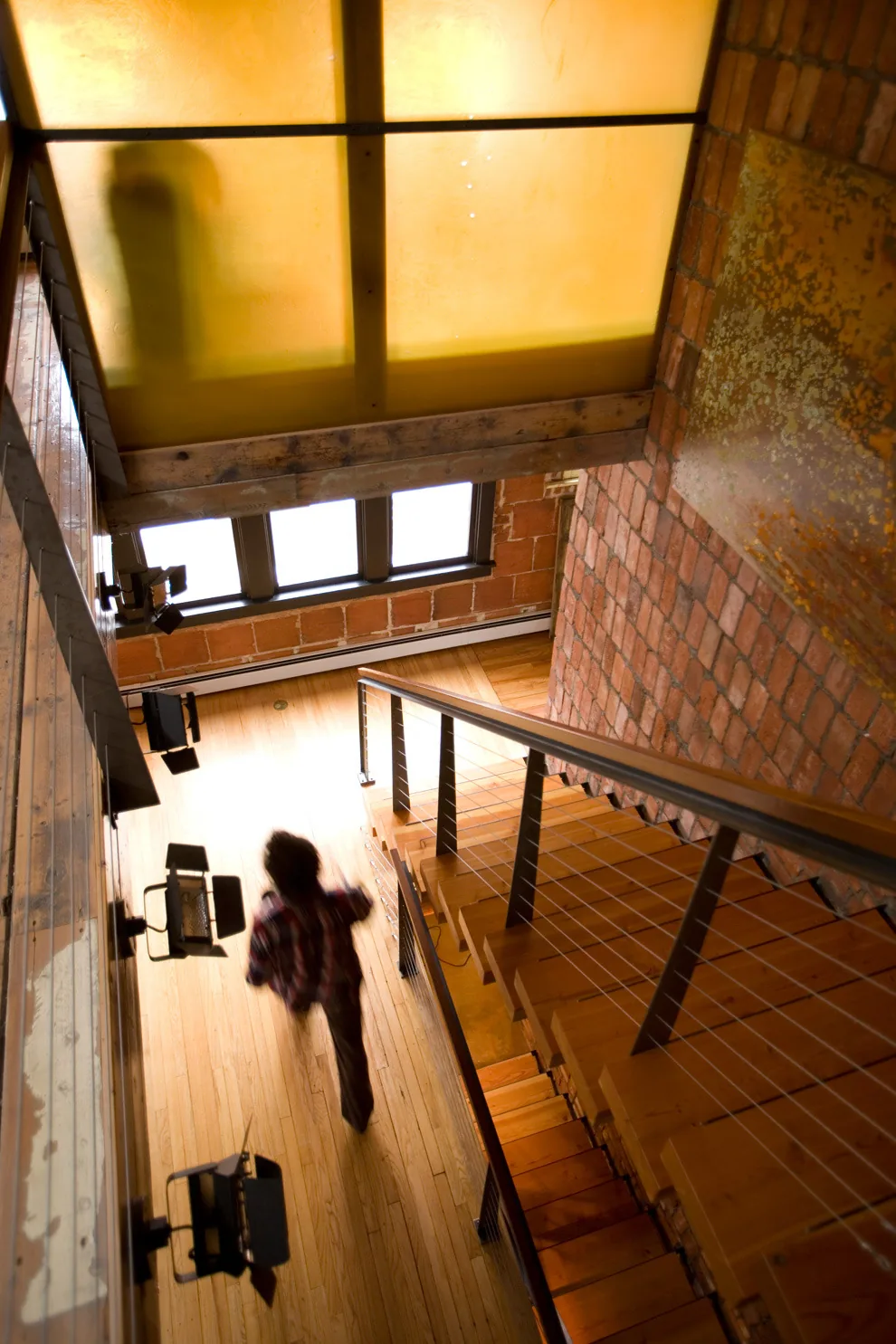 Interior view of a staircase with wood flooring, metal and cable railing, and brick wall details.