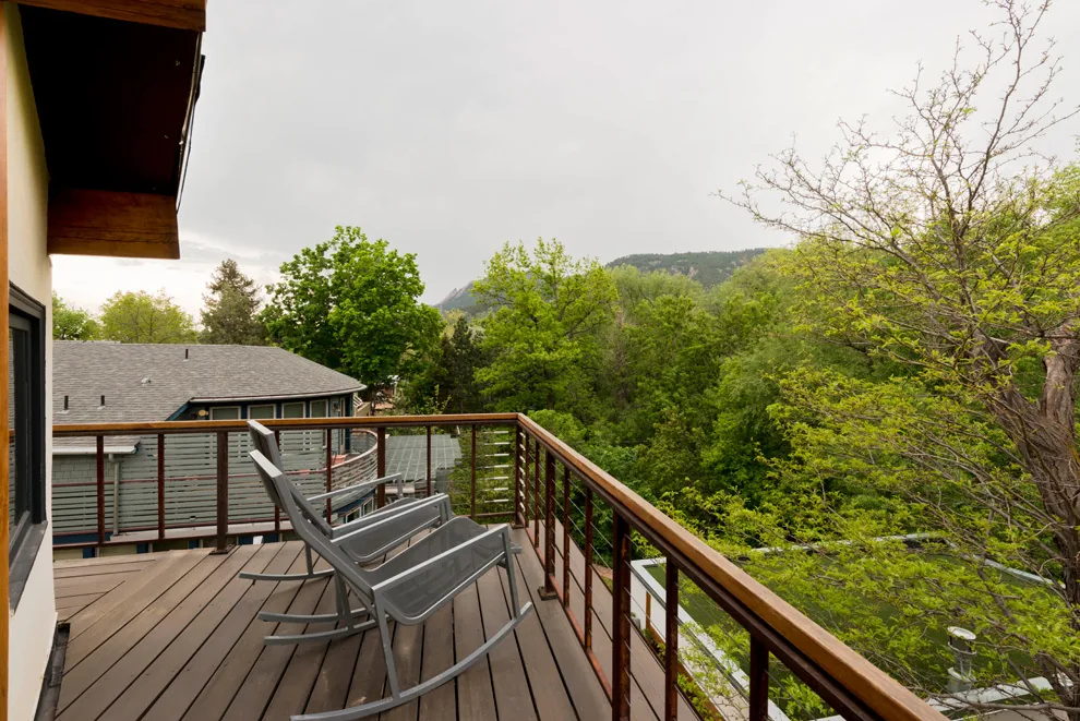 A balcony with metal rocking chairs overlooking a wooded area and adjacent house roof.