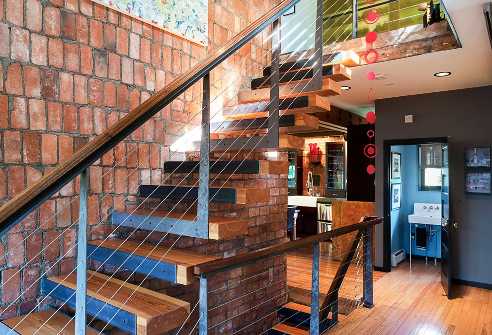Floating wooden staircase with metal railing and brick walls inside a residence.