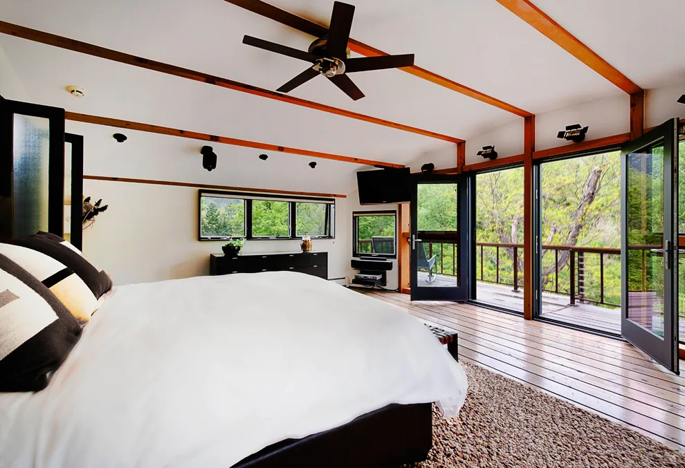 Bedroom featuring exposed beams and floor-to-ceiling glazing opening to an outdoor balcony.