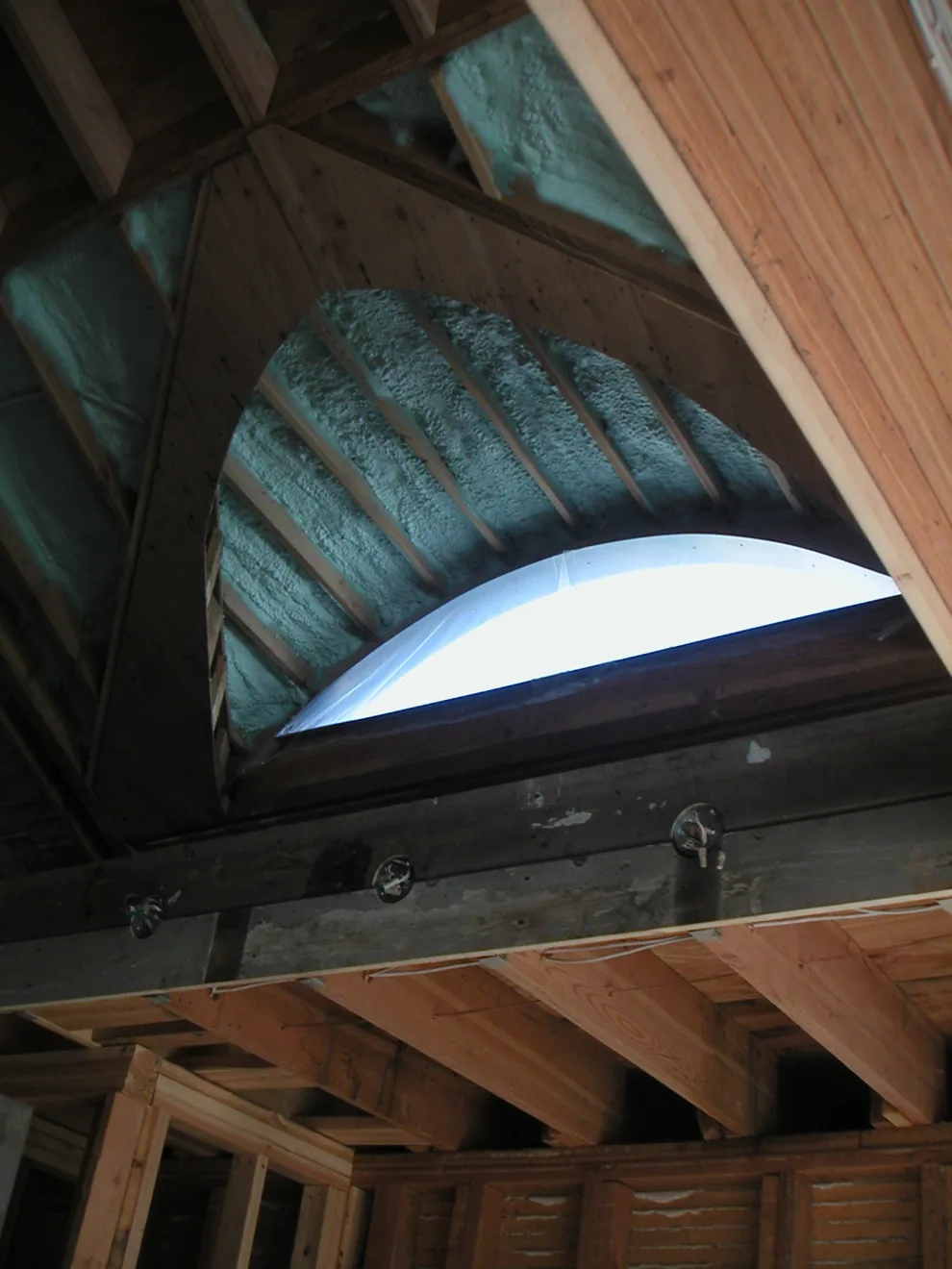 Arched window opening framed within wooden ceiling structure with visible spray foam insulation during construction.