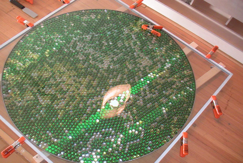 Close-up of a circular glass marble art installation secured with clamps on a worktable.