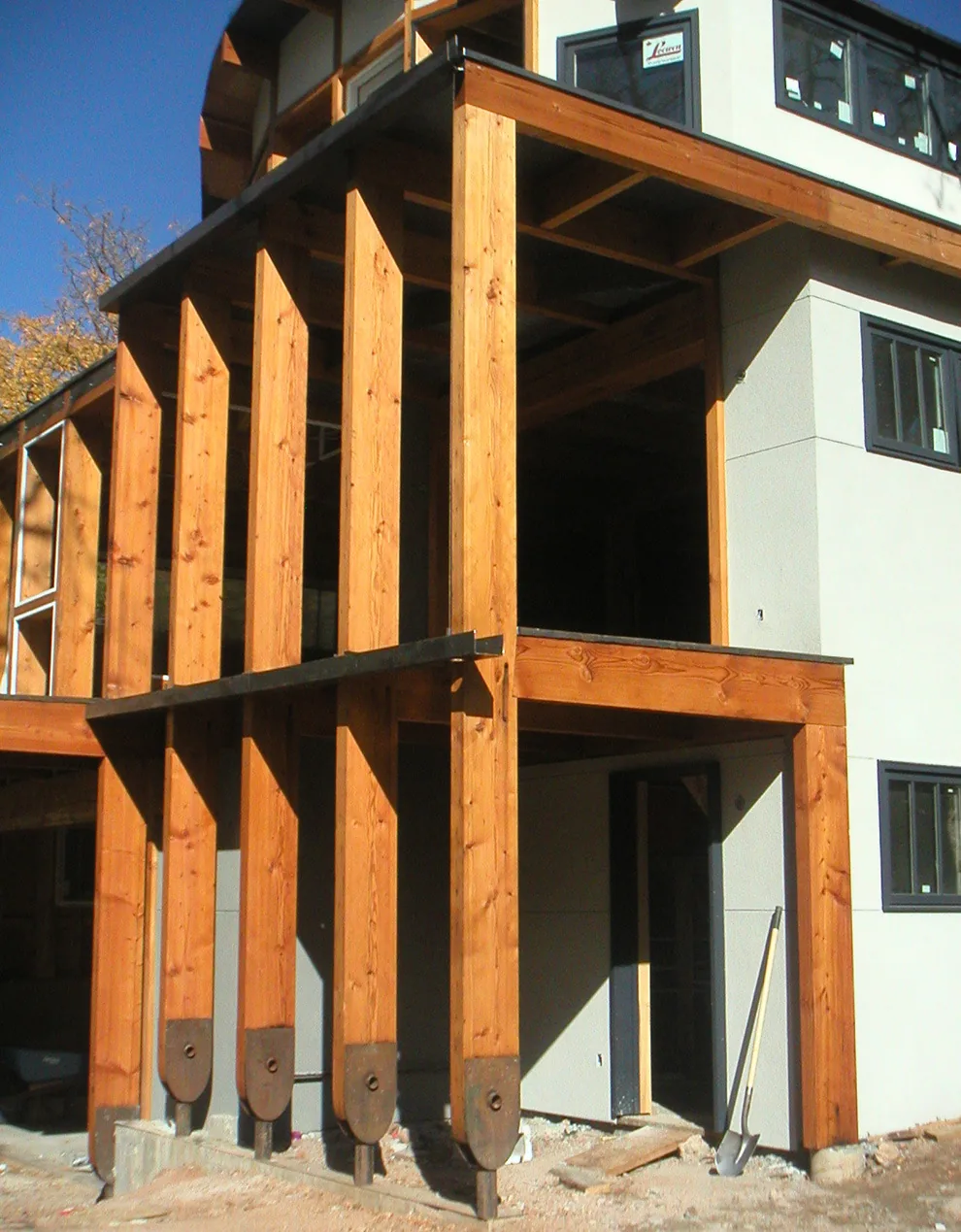 View of the new construction phase showing vertical wood structural beams supporting an upper floor with stucco exterior walls and black-framed windows.