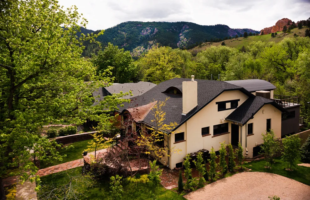 A residential house surrounded by greenery with a mountainous landscape in the background.