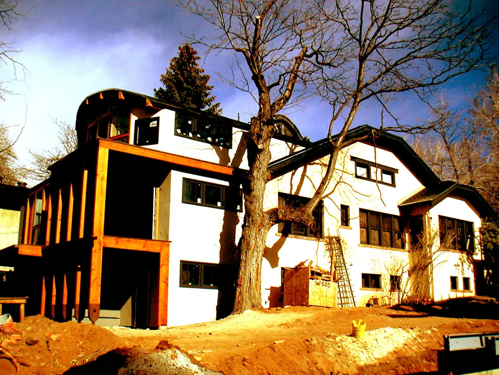 Two-story house exterior under construction with white stucco walls and wood framing details.