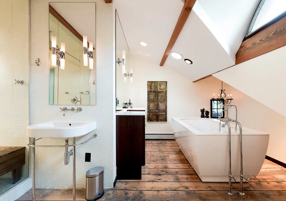 Bathroom features a freestanding tub, wall-mounted sink with chrome fixtures, wood flooring, and skylight windows.
