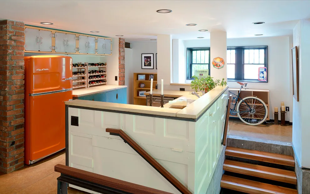 Kitchen area with exposed brick supports and an orange vintage refrigerator adjacent to a stairwell.