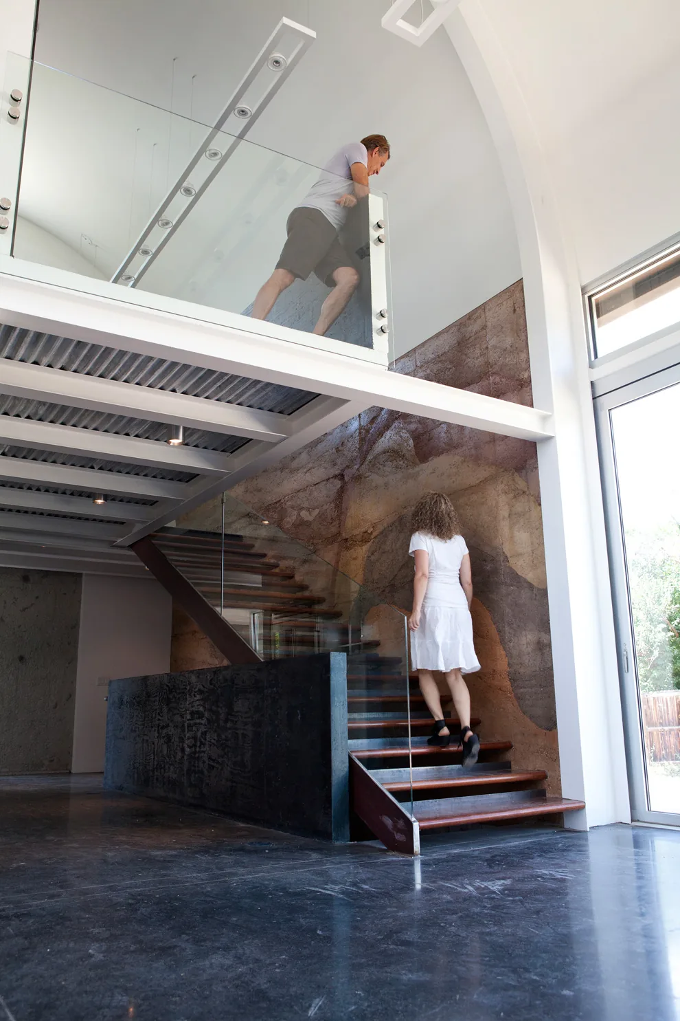 Modern interior staircase with glass railings, wooden treads, and a textured wall finish.