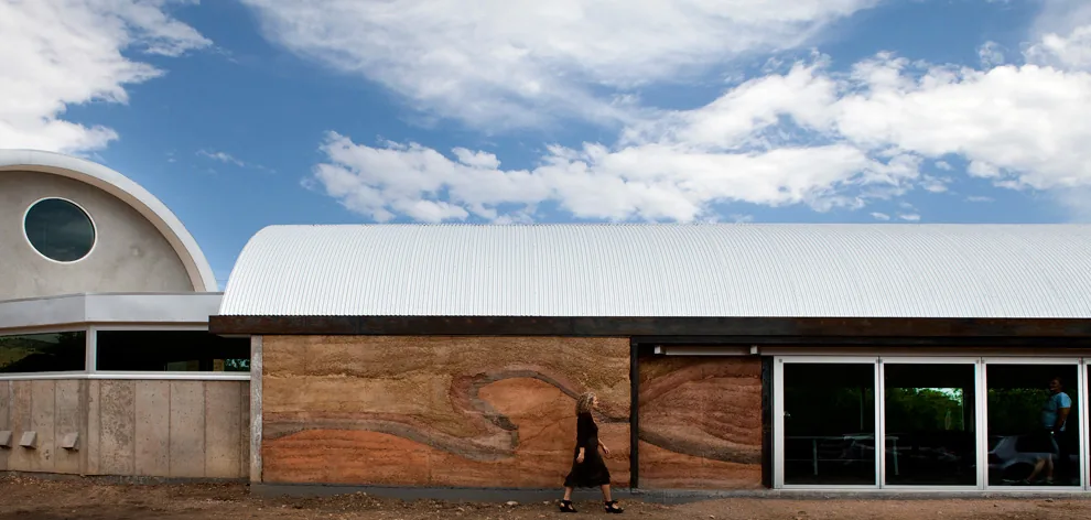 Building exterior with barrel roof, rammed earth walls, and combination of sliding glass and fixed windows.