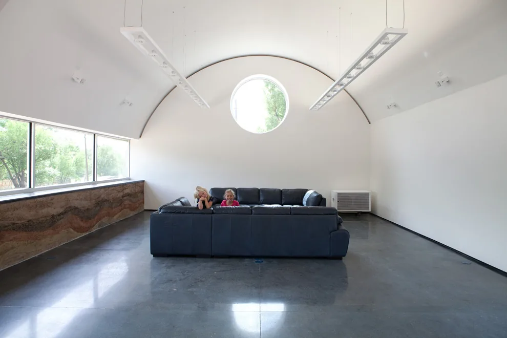 Minimalist living room with vaulted ceiling, circular window, and large sectional sofa.