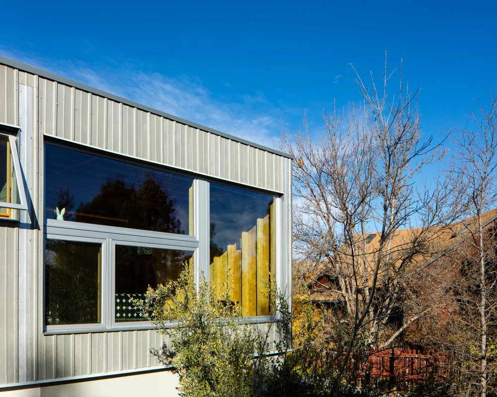 Exterior view of a building facade featuring vertical metal siding and a large window with an open casement section.