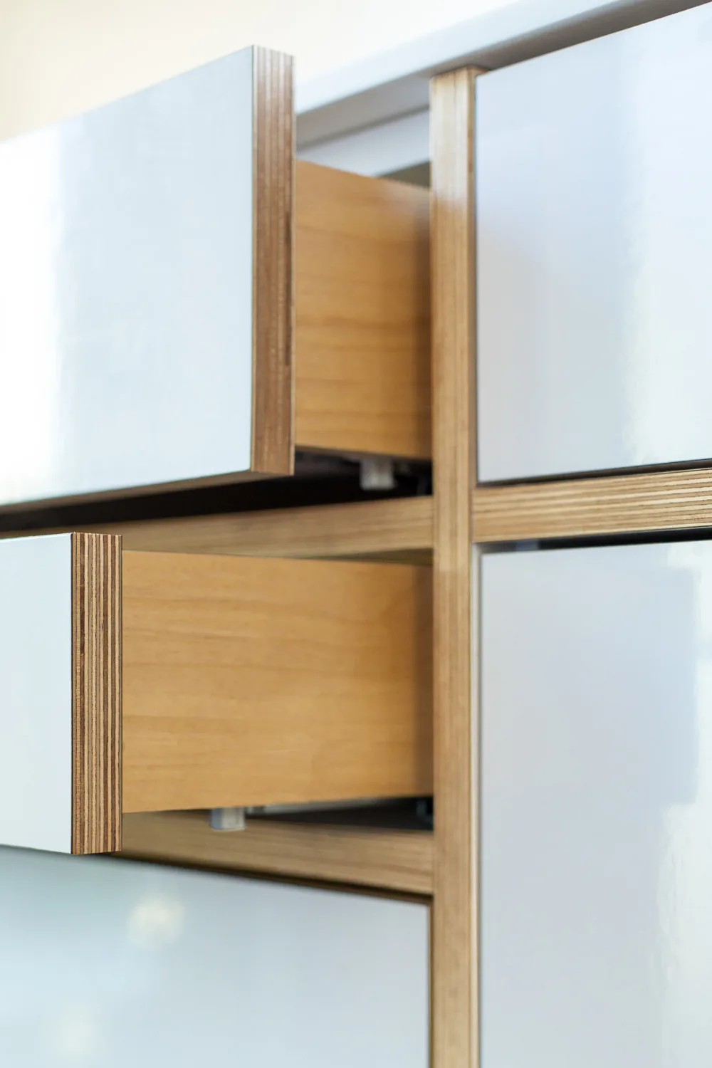 Detail of white glossy drawer fronts with exposed plywood edges in cabinetry.