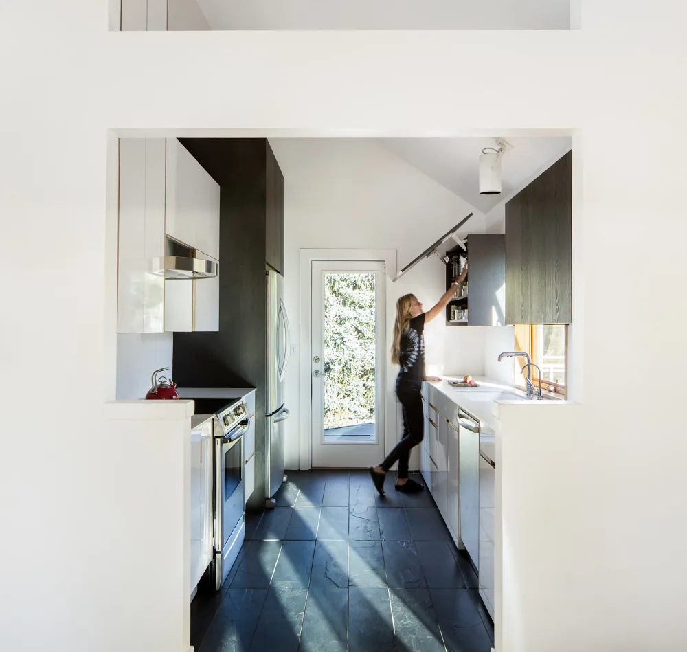 Modern kitchen with a person reaching into an upper cabinet next to a glass door.