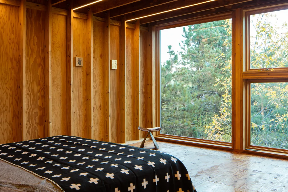 Bedroom interior showcasing exposed wood framing and a large floor-to-ceiling window with a nature view.