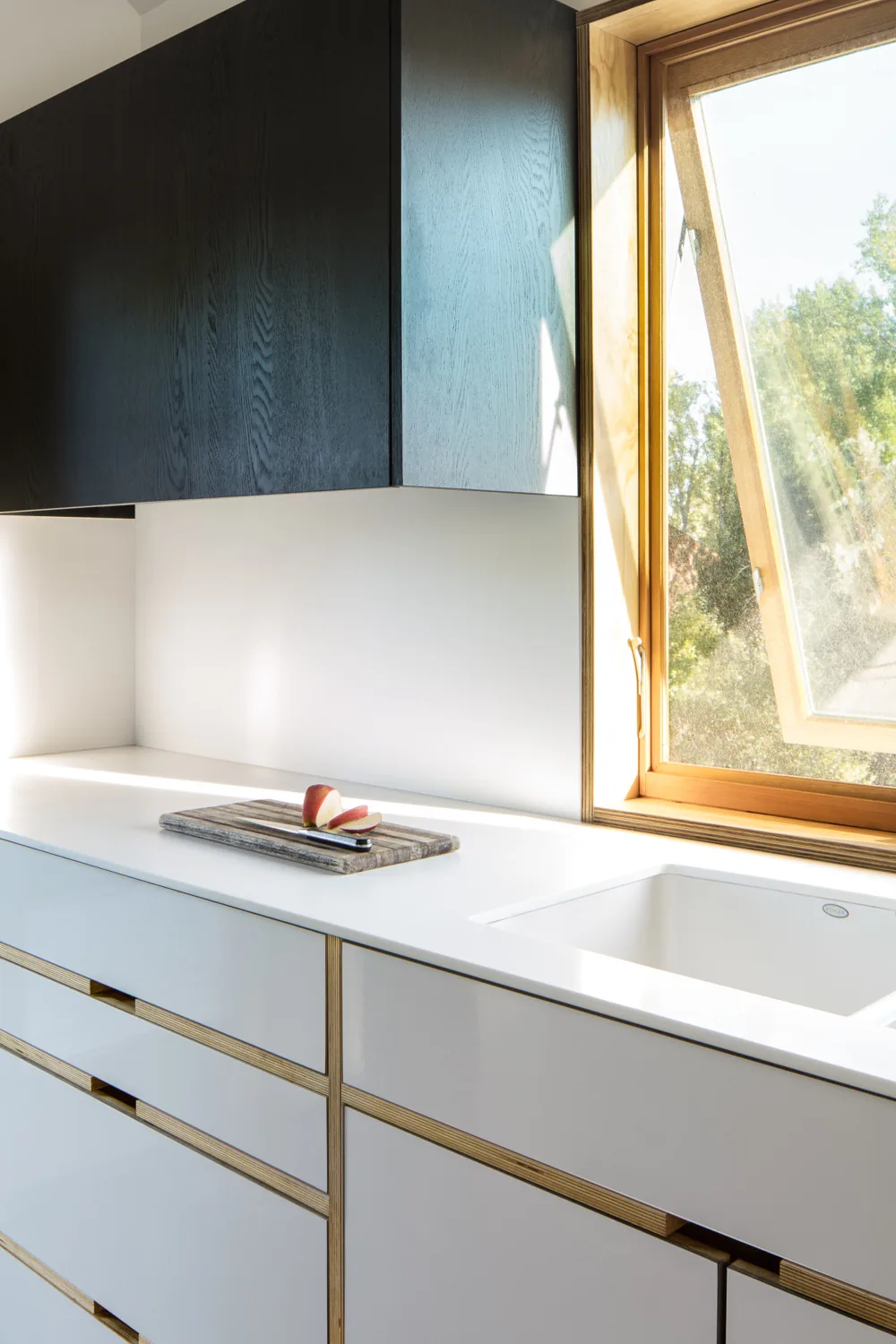 Kitchen countertop with white drawers, wooden upper cabinets, and an open wooden window.