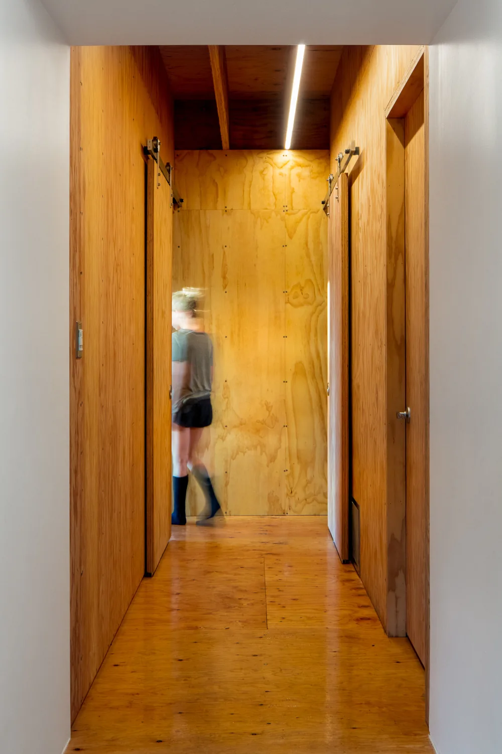 A hallway lined with plywood walls and floors with sliding barn doors on either side.