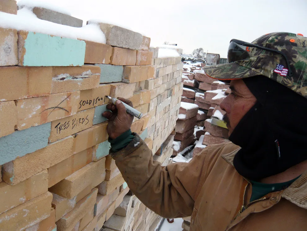 Worker marks bricks with notes on a snow-dusted construction site.