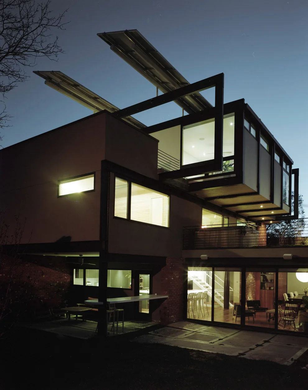 The QUIVAS house features cantilevered volumes with large windows and exposed structural steel framing at night.