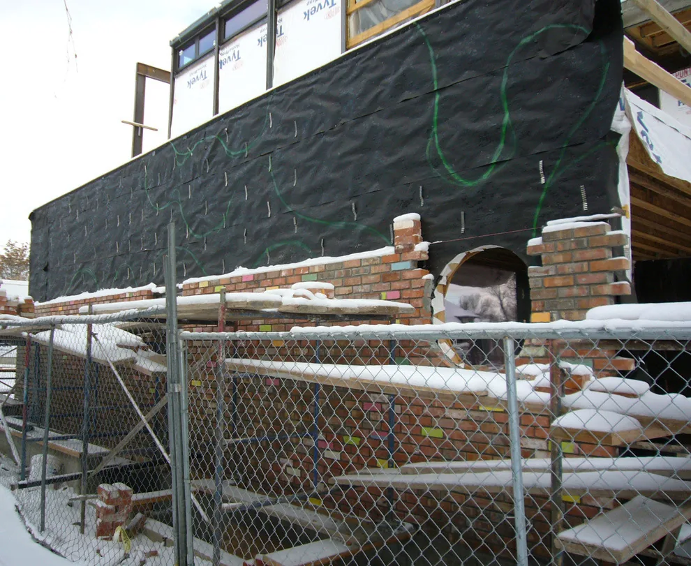 Building exterior wall under construction with brick veneer and a circular window opening in winter conditions