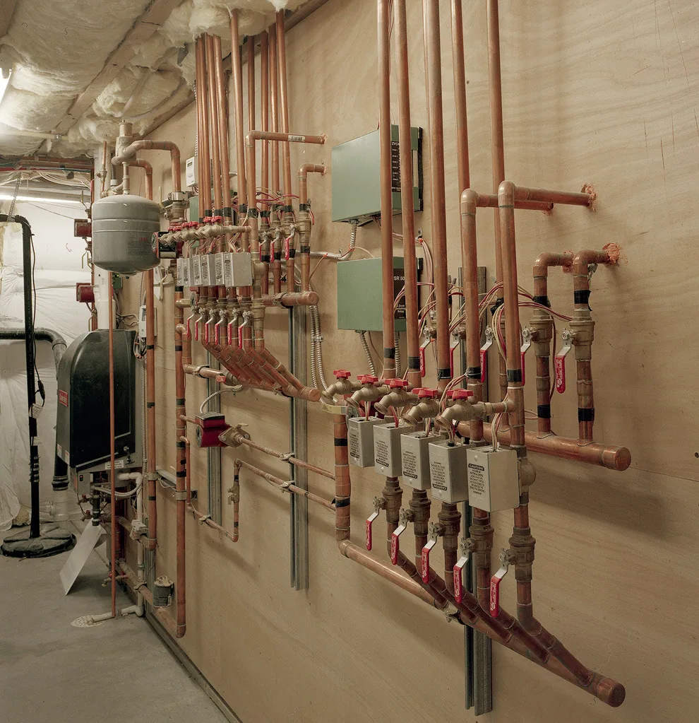 Mechanical room featuring copper piping with multiple valves and control boxes mounted on a plywood wall.
