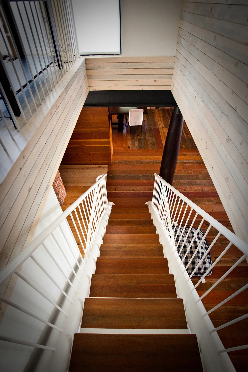 Interior view looking down a wooden staircase with white railings and light wood paneling on walls.